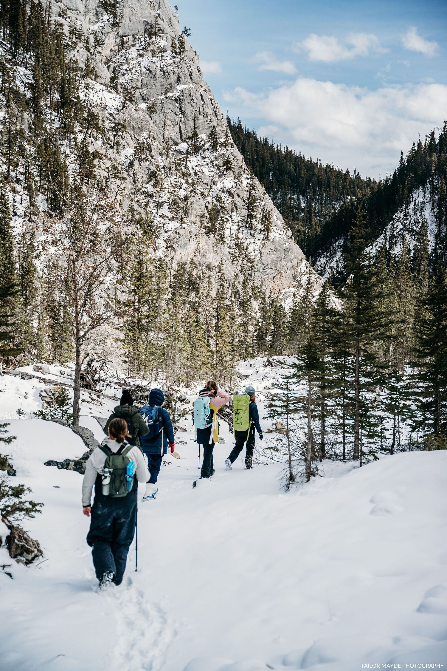 Winter hikers following a snowy trail through a dramatic mountain canyon.