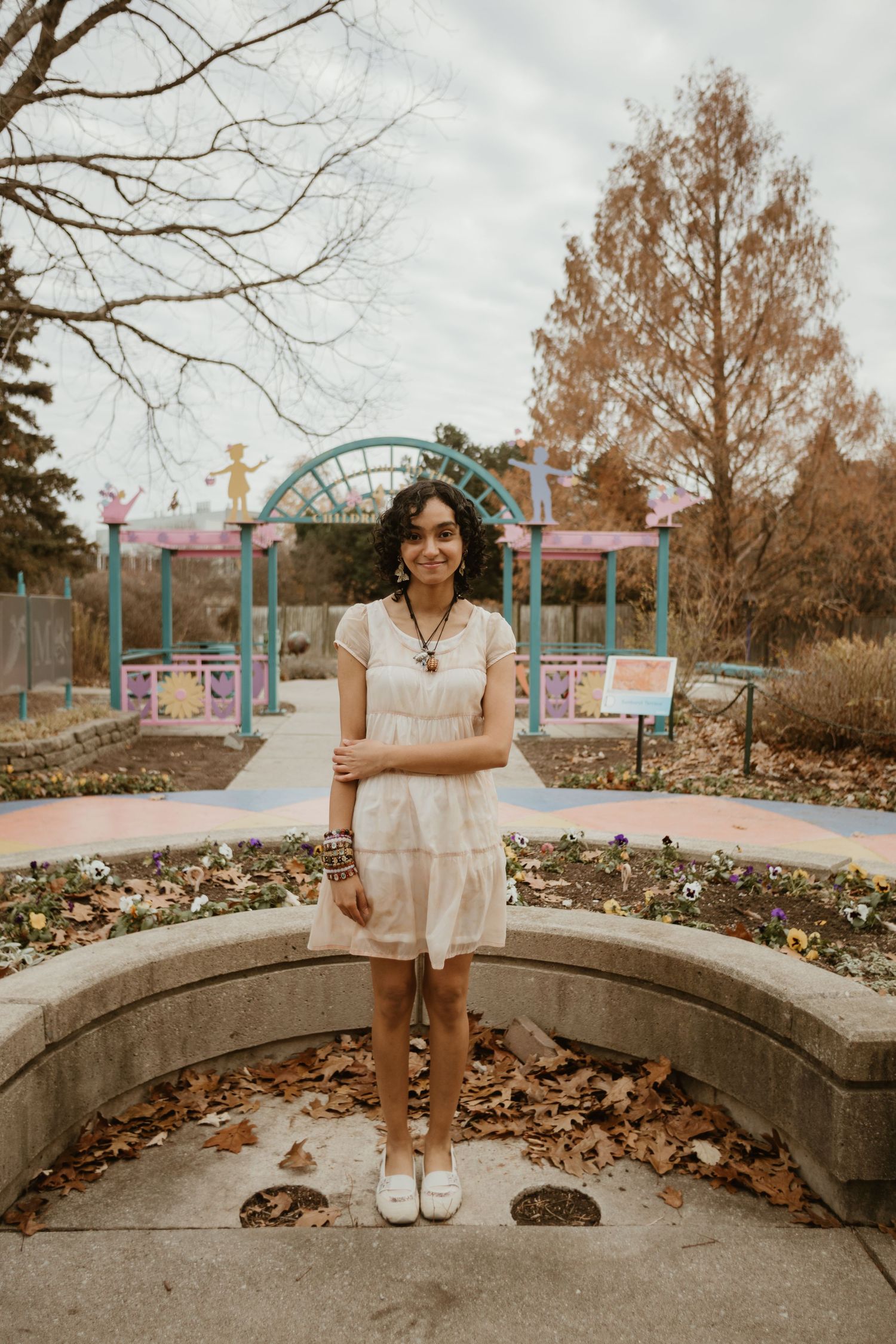 A series of photos showing someone in a white dress sitting and standing on a curved stone wall surrounded by autumn leaves.