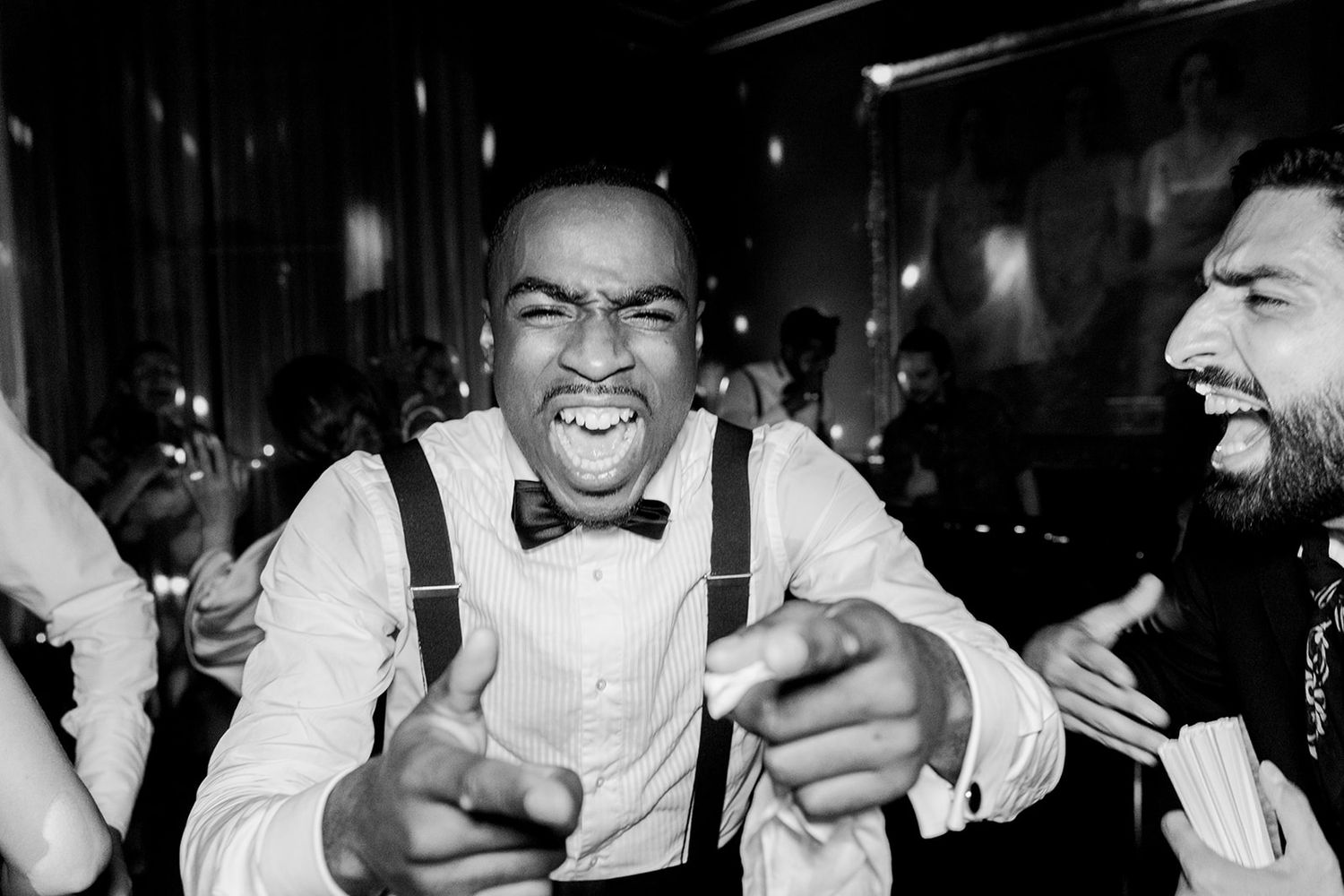 Black and white photo showing people laughing and celebrating at a formal event with bow ties and white shirts.