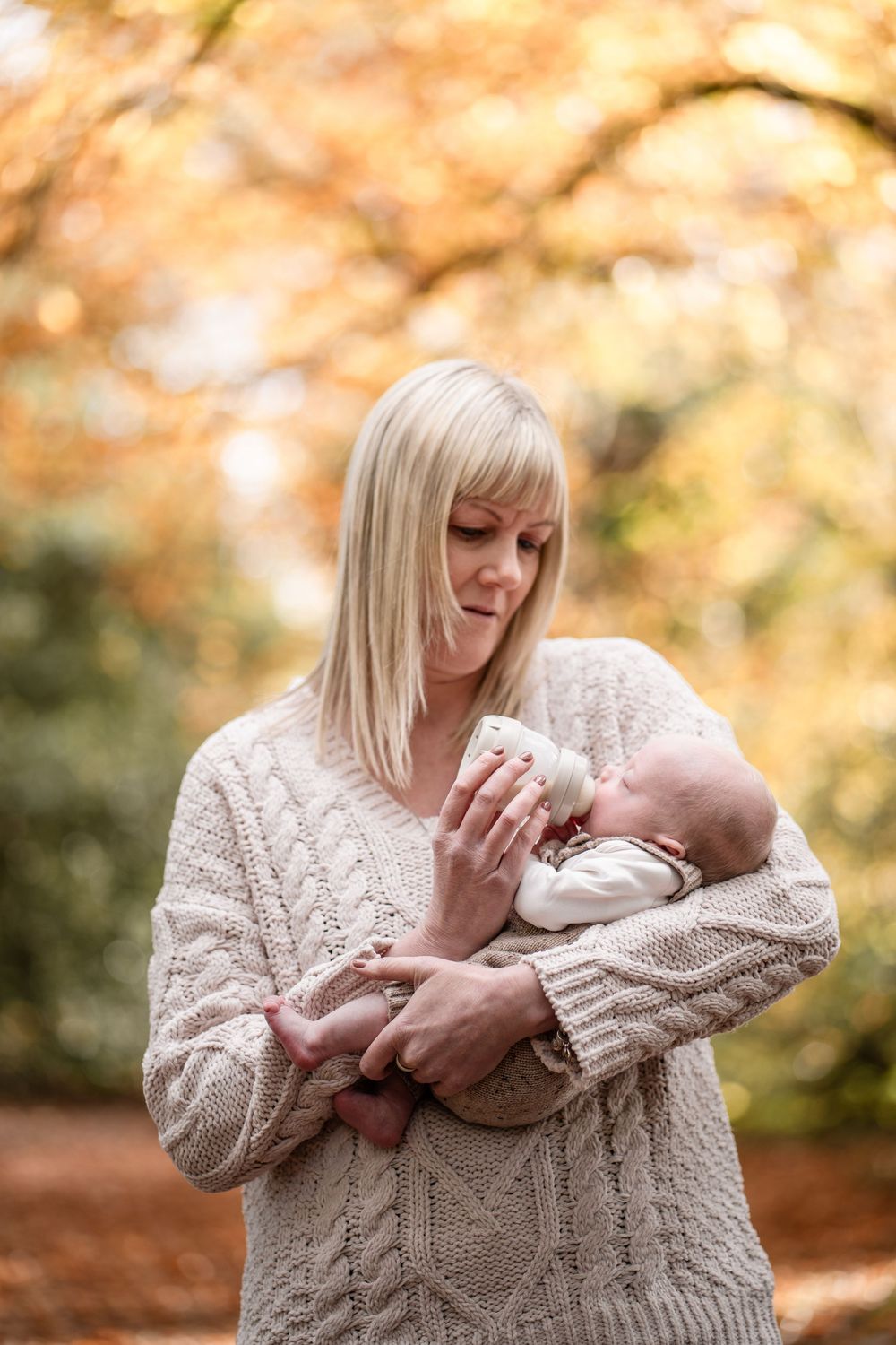 A tender moment between parent and baby in matching cream knit sweaters surrounded by warm autumn foliage.
