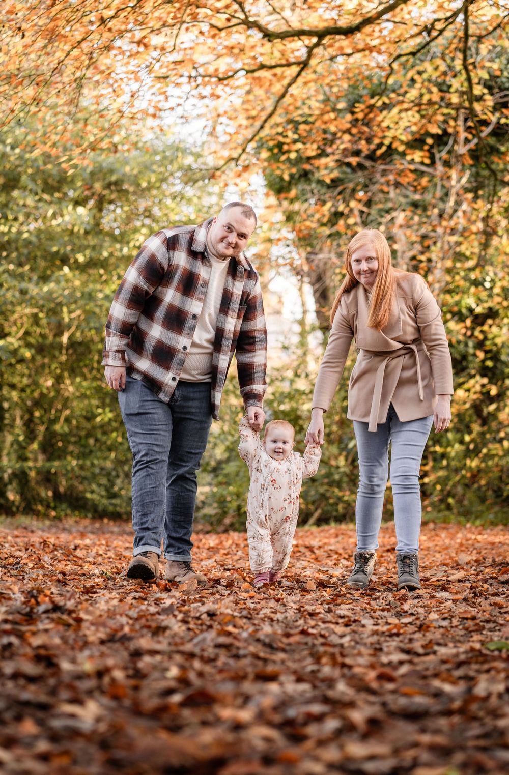 Family members walking together through fallen autumn leaves on a forest path.