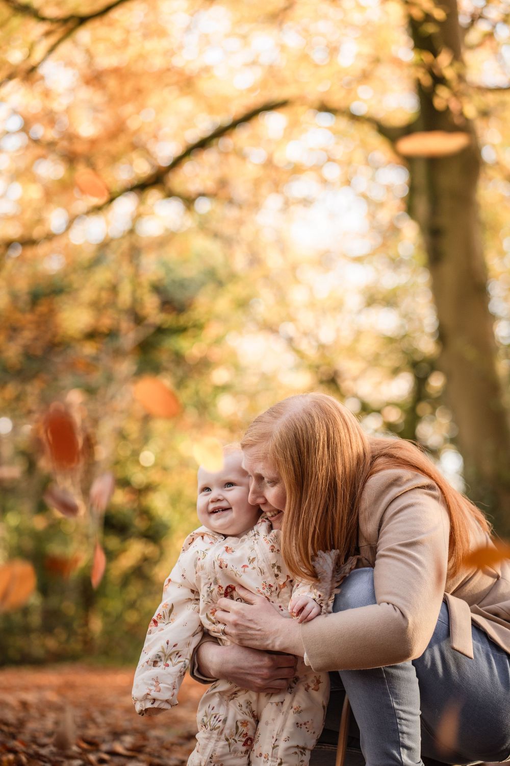 A tender moment between parent and child playing in a park during autumn with golden leaves in the background.