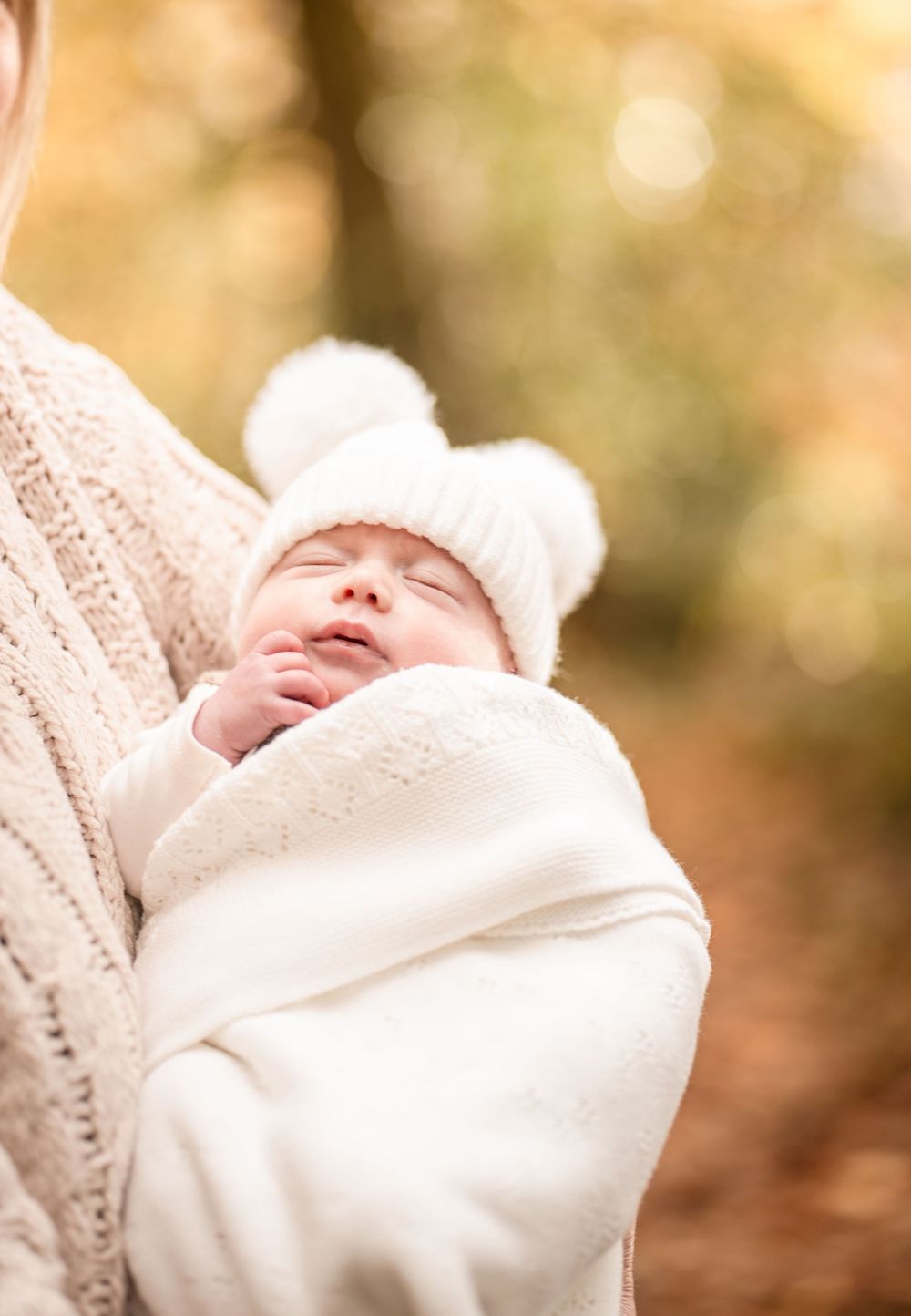A sleeping newborn baby swaddled in white blankets against a soft bokeh background.