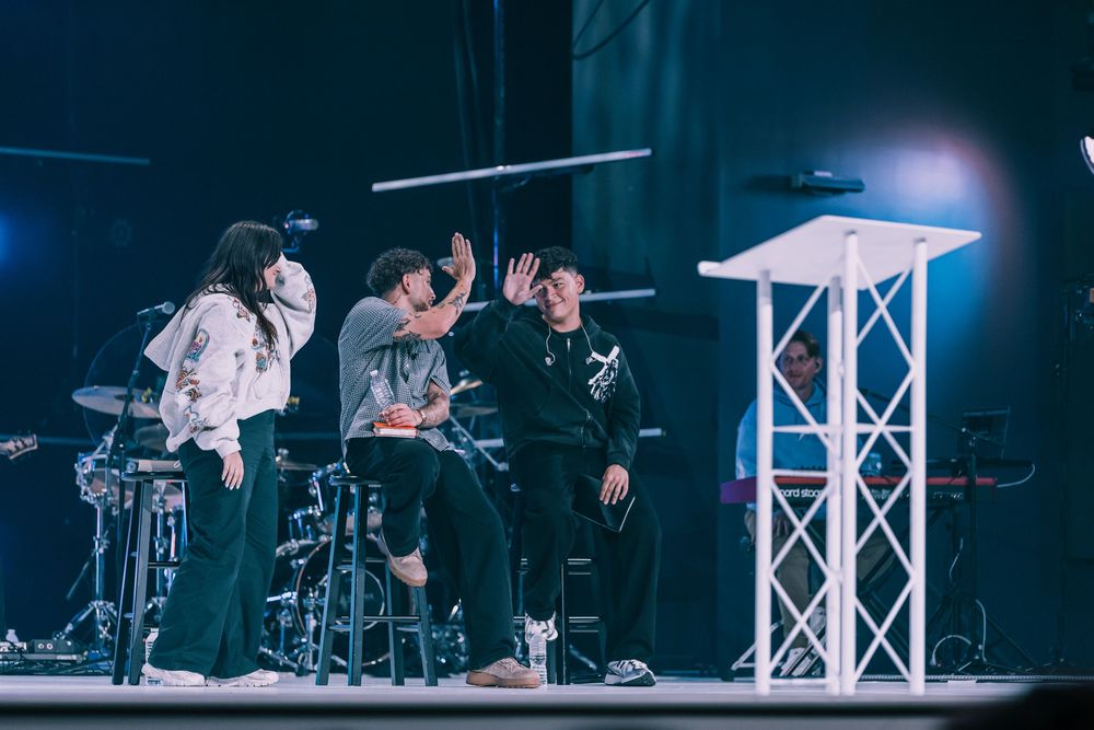 Three people high-fiving on a church stage with a white podium in the background.