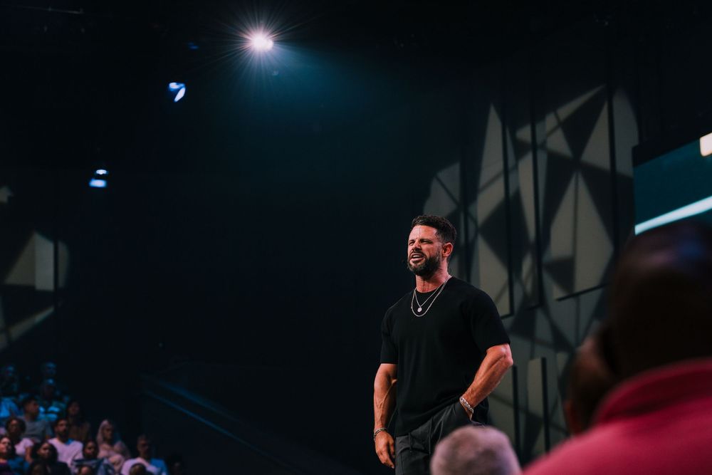 Man in black shirt and jeans standing confidently on a large church stage.