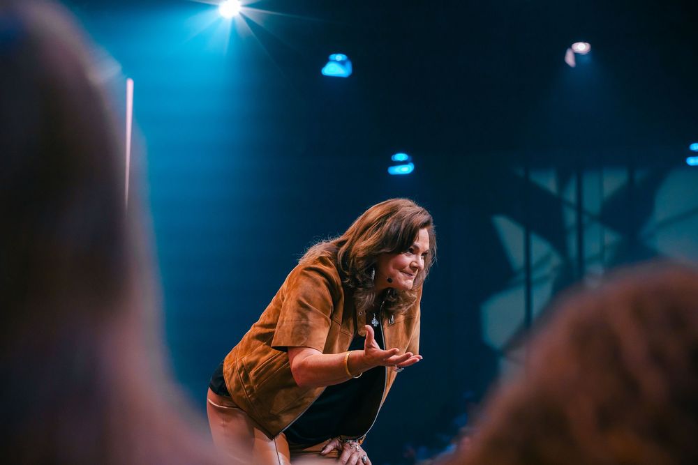Female performer leaning toward audience on stage with dramatic blue lighting at live music event.