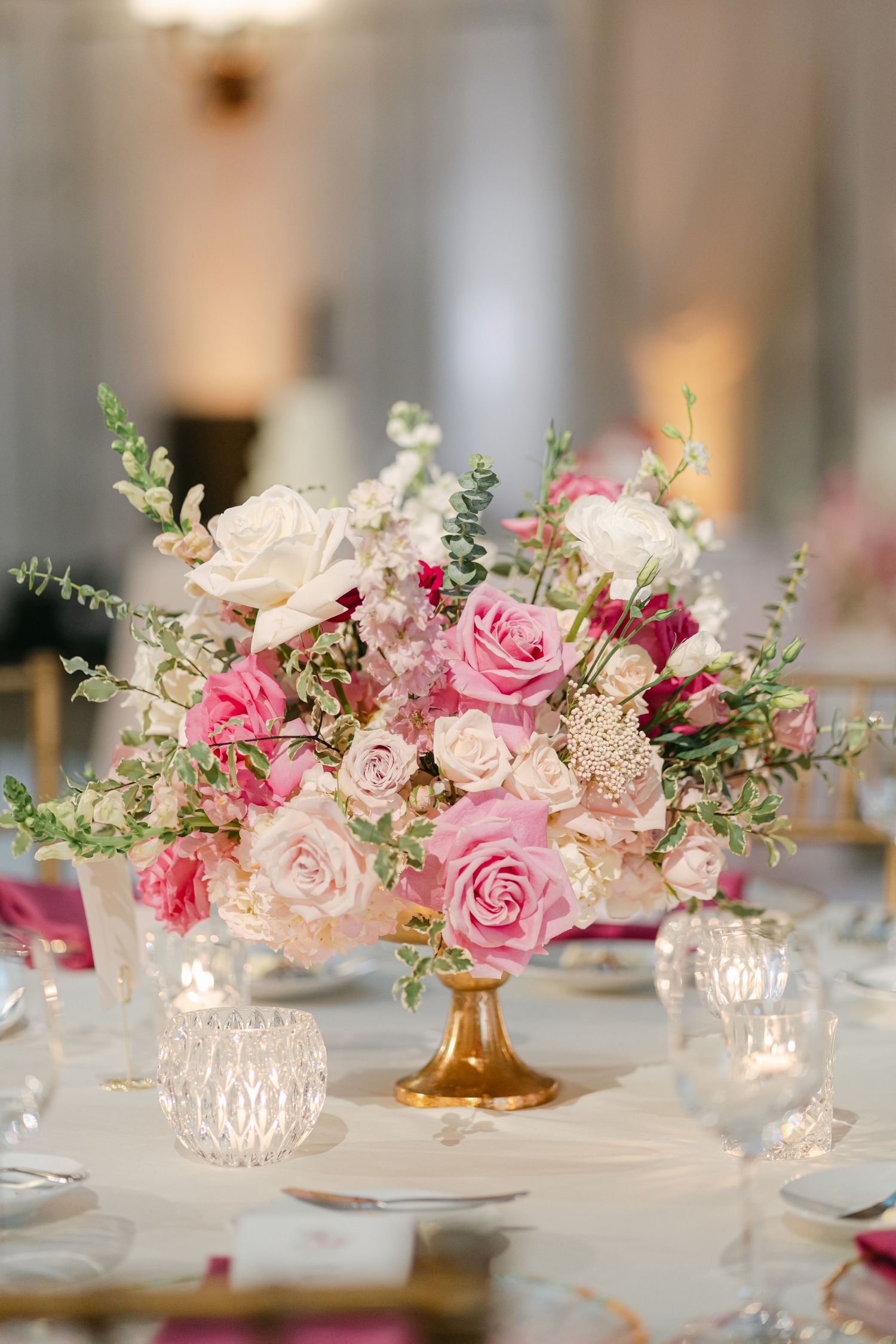 Elegant wedding reception table setting with pink rose centerpieces and crystal votives on white tablecloths.