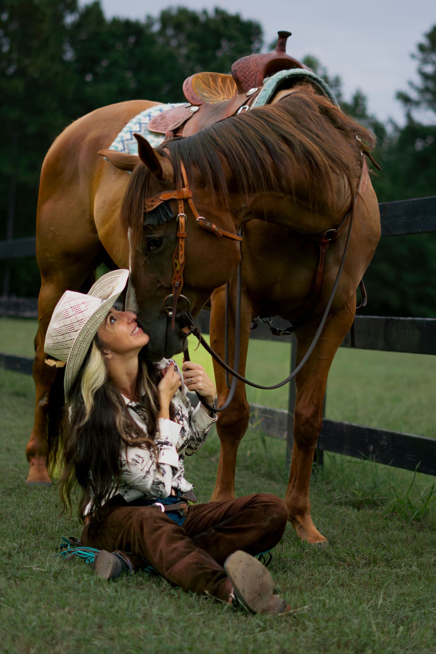 Person sitting on ground in front of horse while horse puts their head in persons lap.