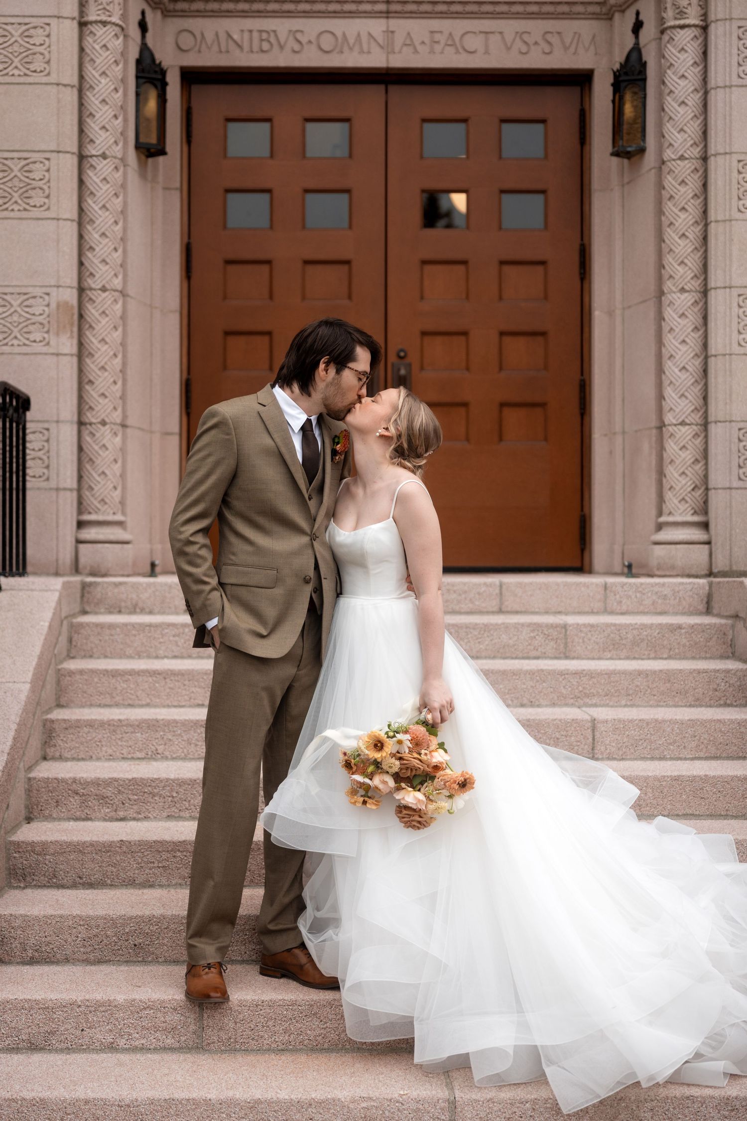 A wedding couple shares romantic moments in front of a grand stone building with wooden doors.
