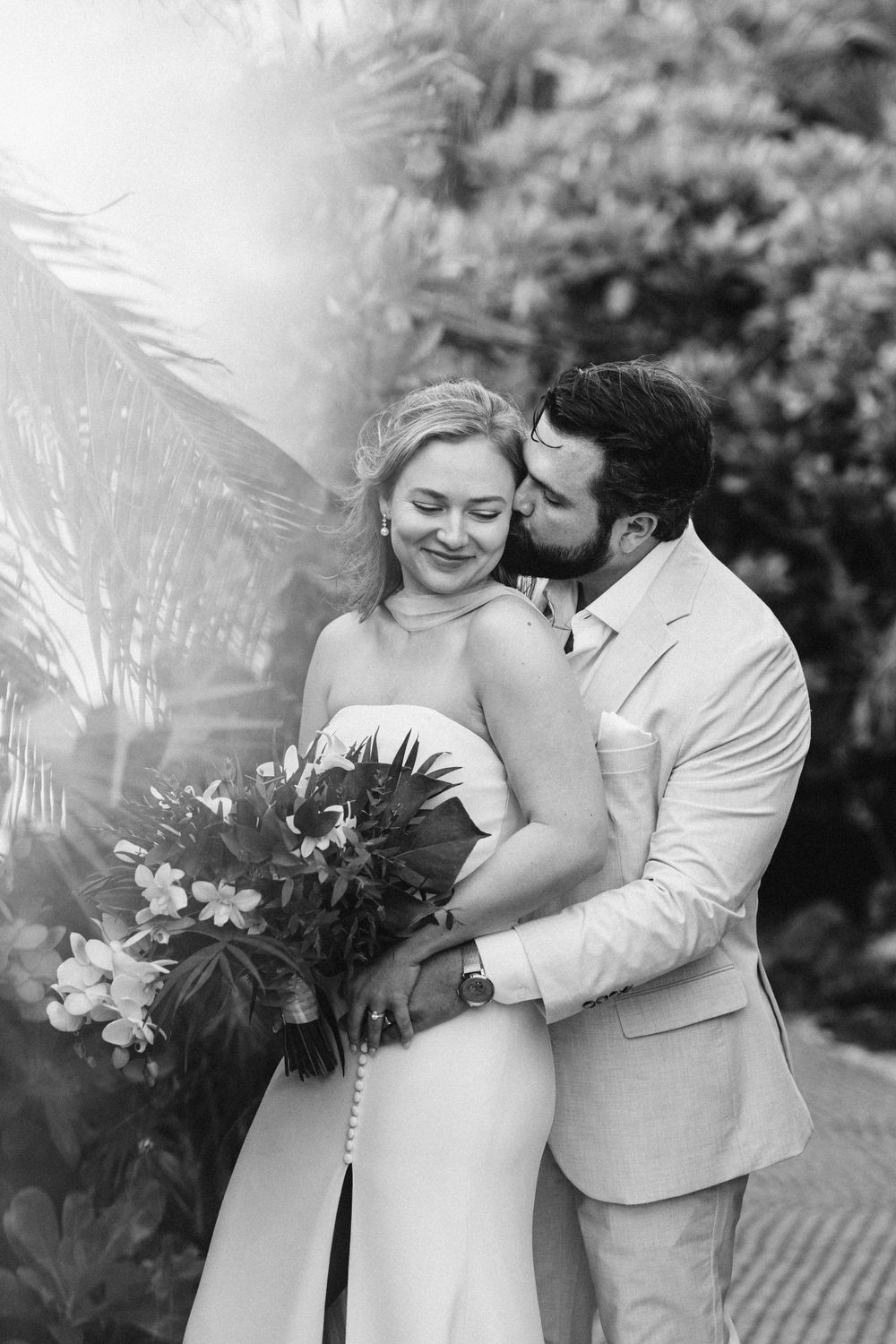 A couple shares an intimate embrace in a garden setting during their black and white wedding photoshoot.
