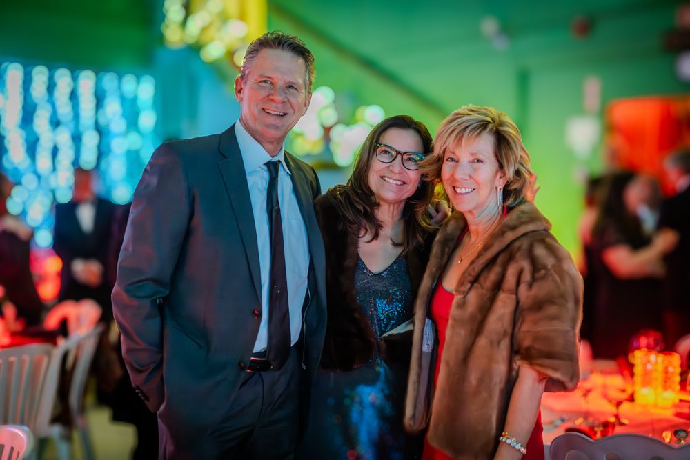 People gather at an elegant evening event with colorful lighting in a festive indoor venue.