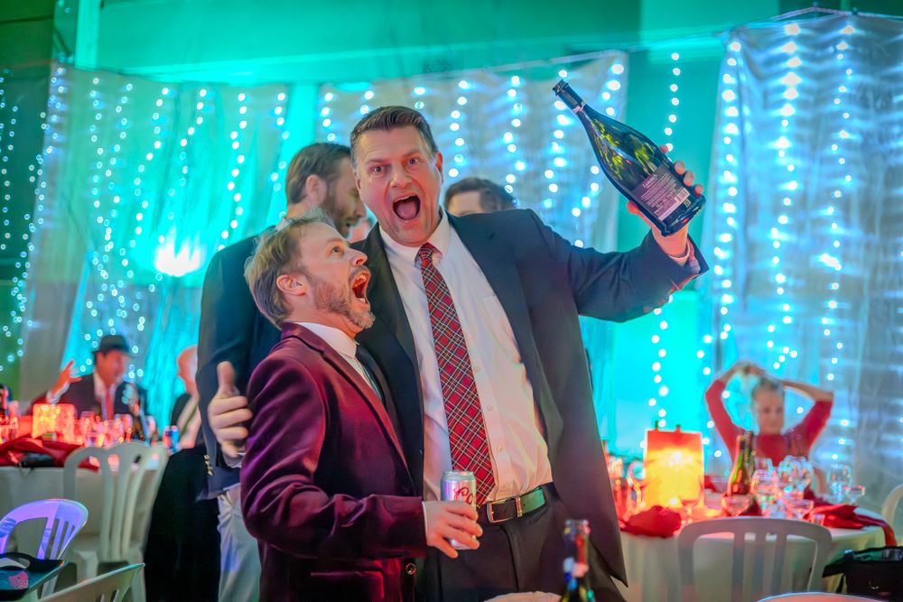 Lively party scene with two people celebrating enthusiastically under turquoise lighting and string light decorations.