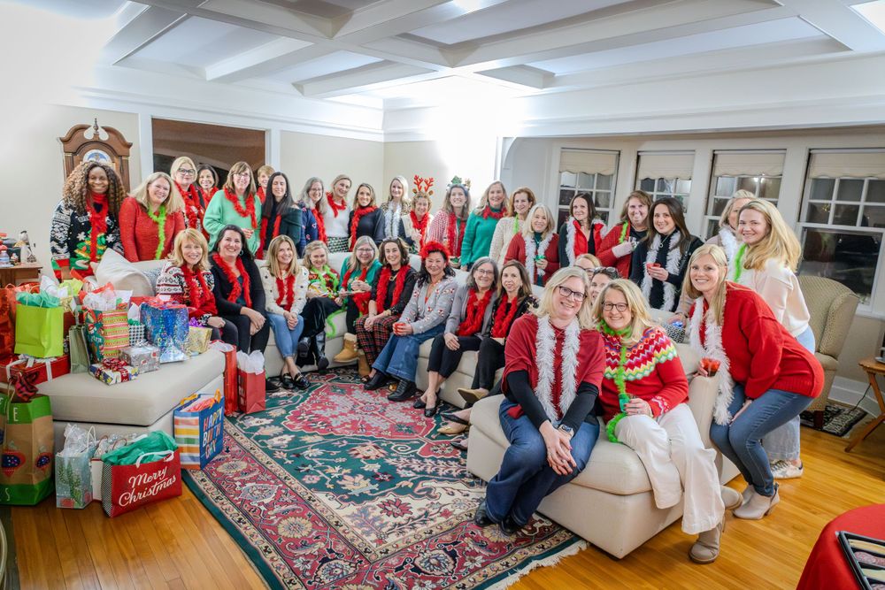 A large group of people in festive red and white holiday attire gather around wrapped presents at a Christmas party.