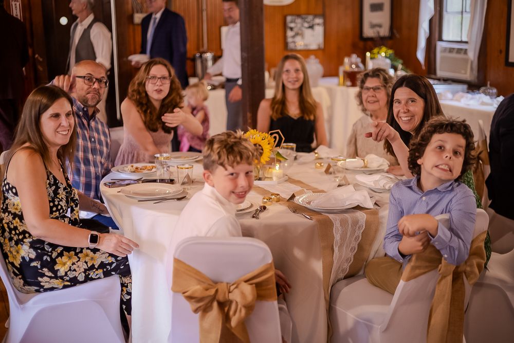 Guests seated at a round table with beige linens and gold bows during a formal dining event.