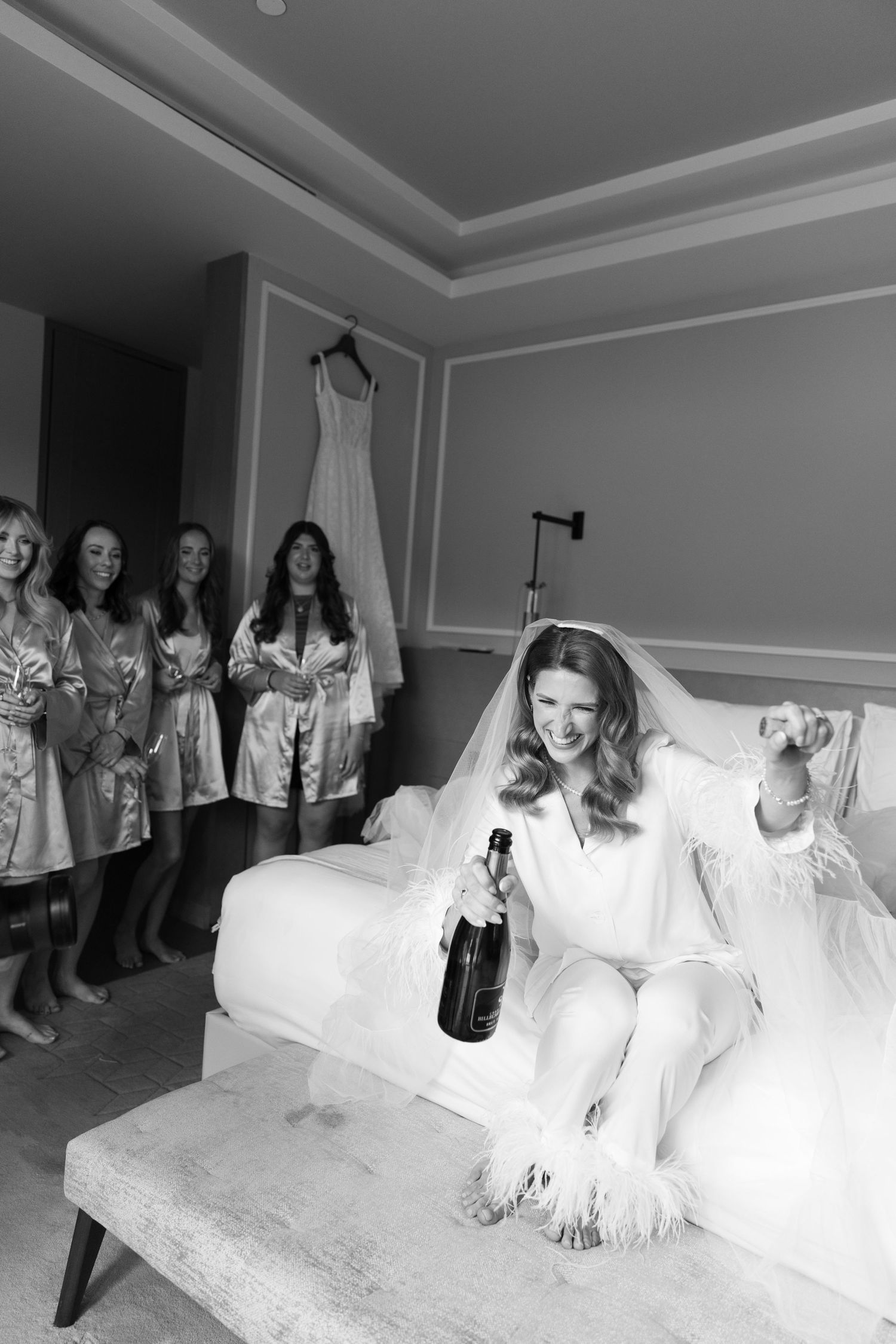 A bridal party relaxes with champagne in a hotel room before the wedding ceremony in black and white photography.