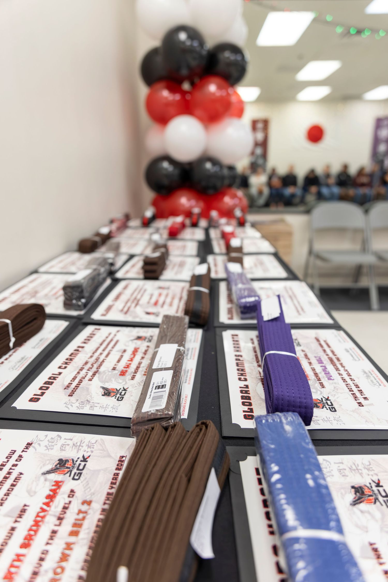 Certificates and documents laid out on a table with red, white and black balloon decorations in the background from a Karate Graduation.