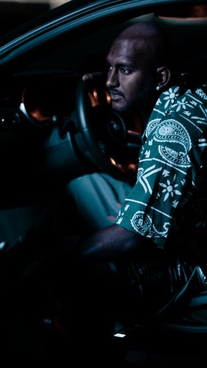 Person in patterned shirt sitting in driver's seat of car at night.