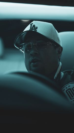 Driver wearing white baseball cap and glasses illuminated by cool toned car interior lighting.