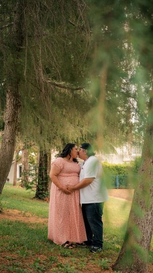 A loving couple embraces under a weeping willow tree in a park, with soft sunlight filtering through the branches.
