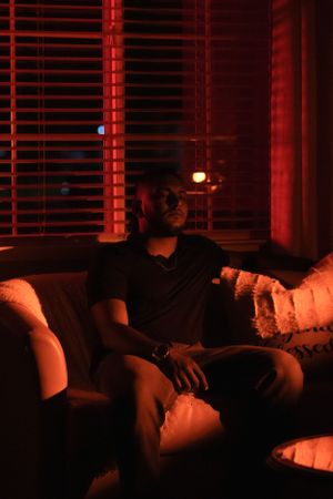 Person seated on couch in dimly lit room with red ambient lighting.