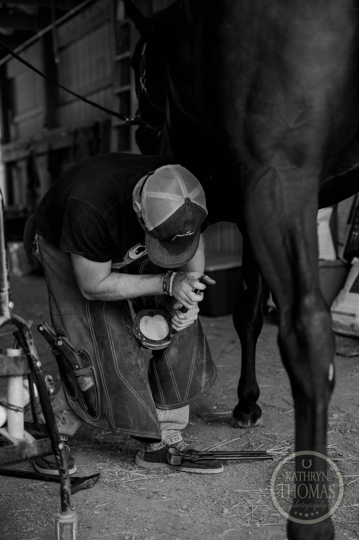 Black and white photo of farrier performing hoof maintenance on horse.