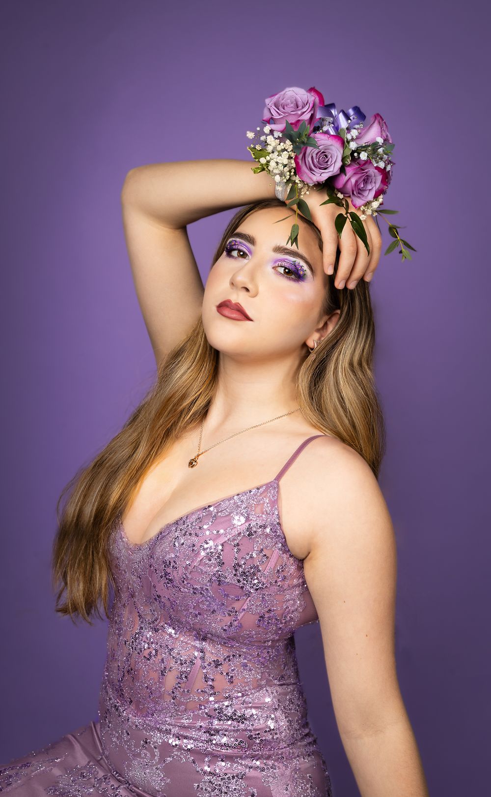 Woman with purple dress and purple flowers with matching makeup, in front of a purple backdrop.