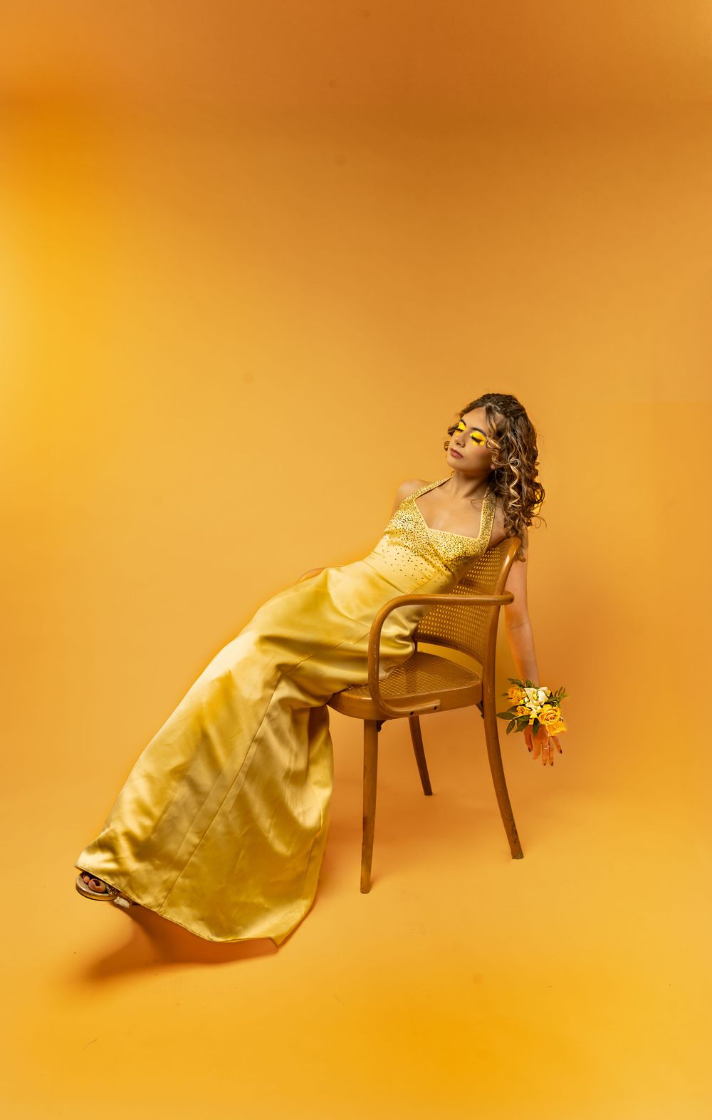 Woman with yellow dress and yellow flowers with matching makeup, in front of a yellow backdrop.