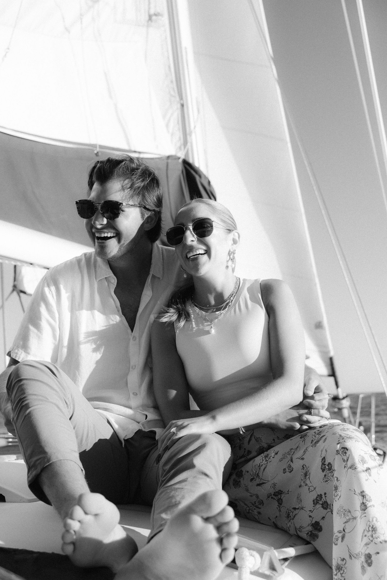 Black and white photo of two people laughing together on a sailboat.