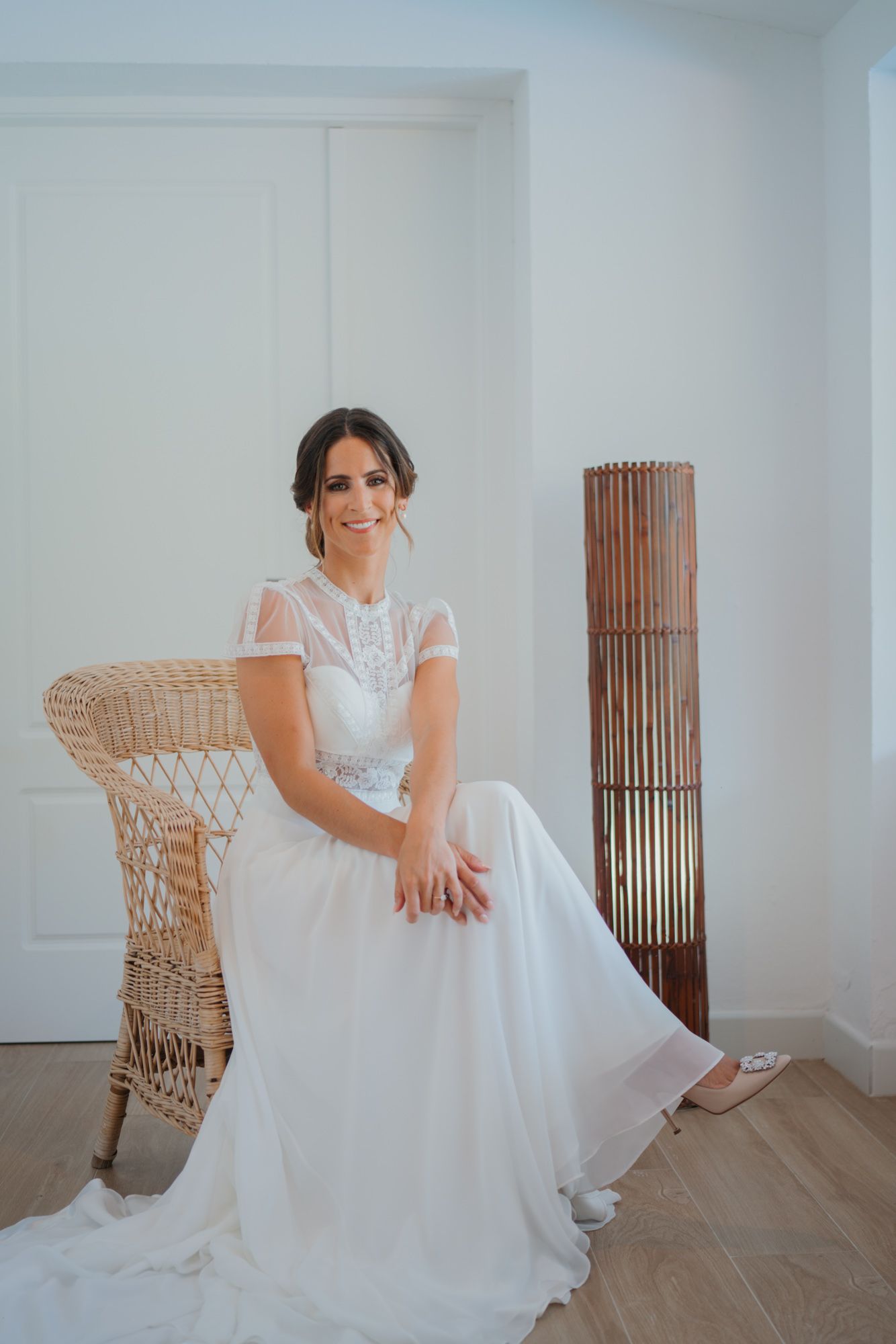 Classic bridal portrait with woman seated in wicker chair against white wall.