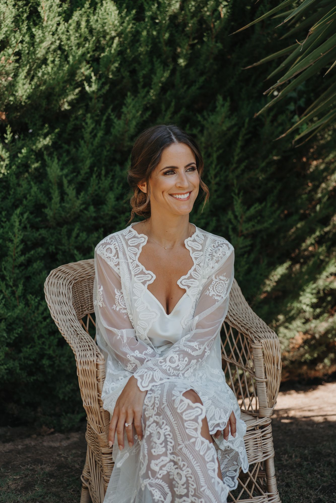 Beautiful lace wedding dress shown in outdoor garden setting with wicker chair.