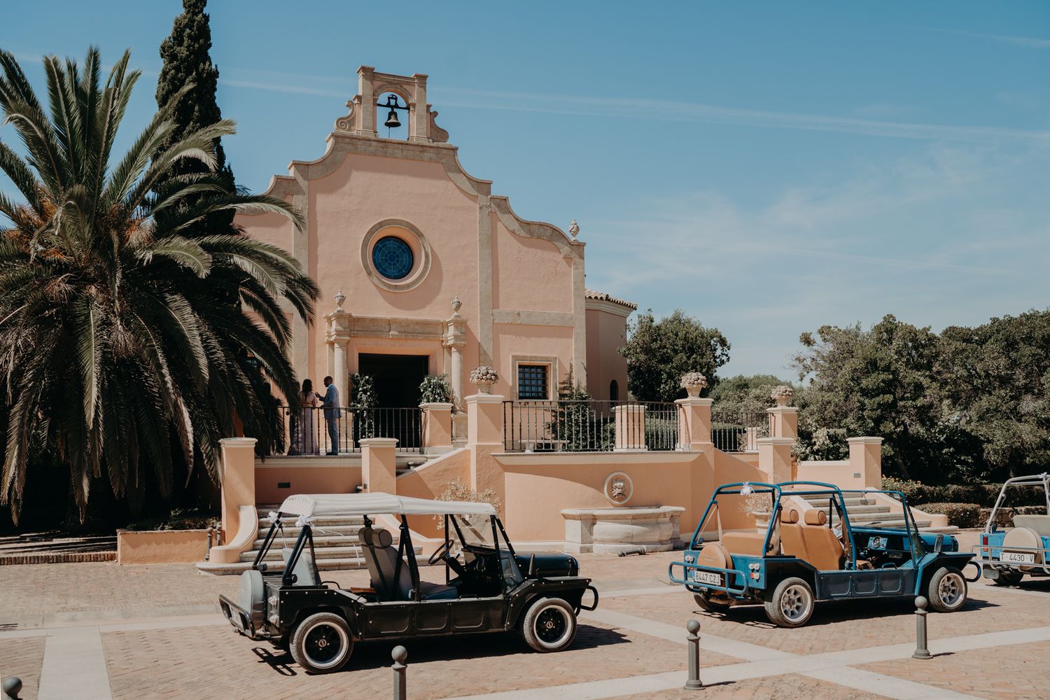 Historic Spanish mission style church with palm trees and classic cars parked outside.