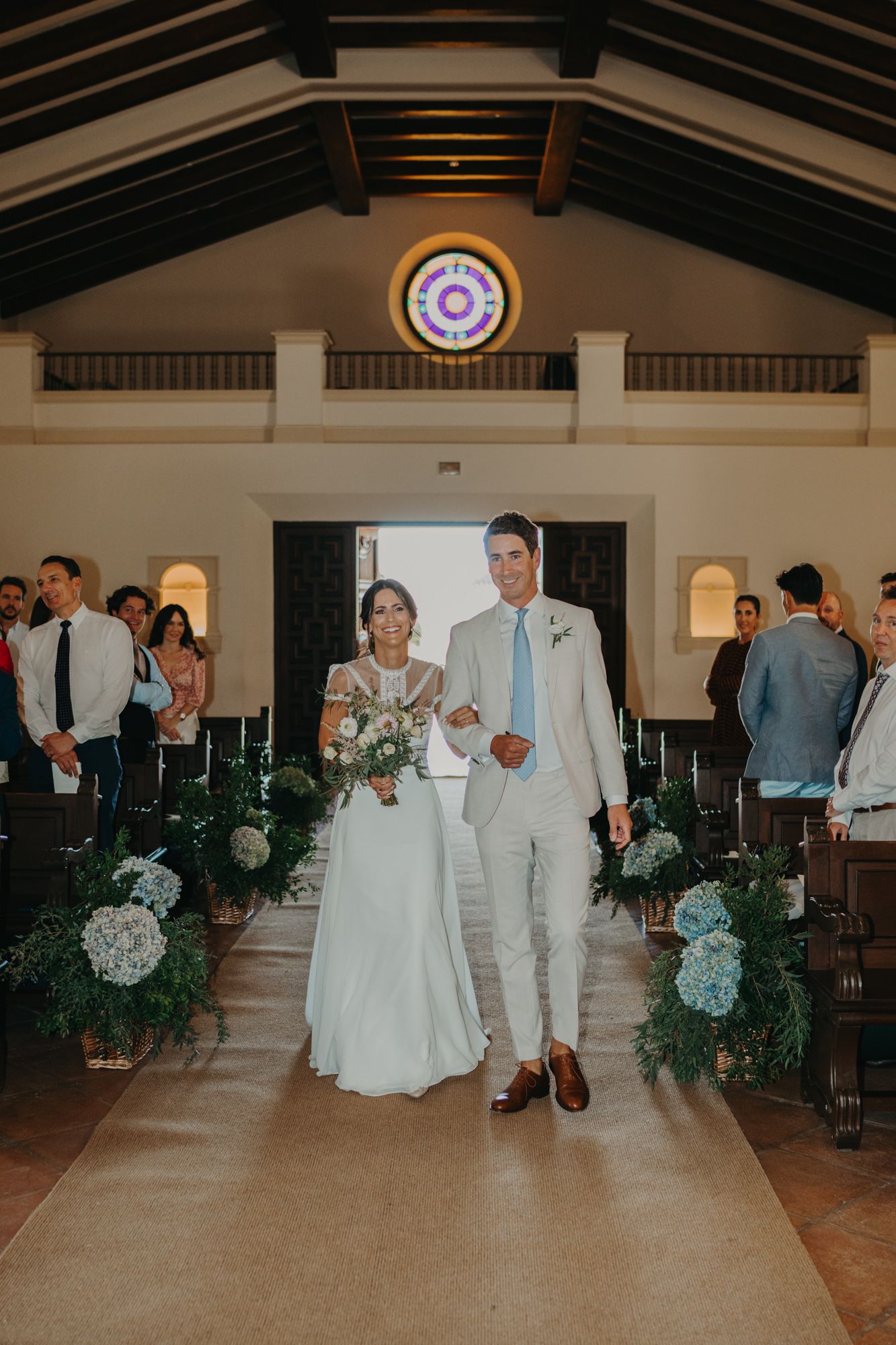 A wedding ceremony at a church with decorative floral arrangements along the aisle.