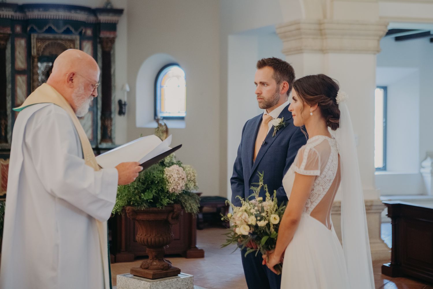 A wedding ceremony in progress inside a traditional church with arched windows and stone walls.