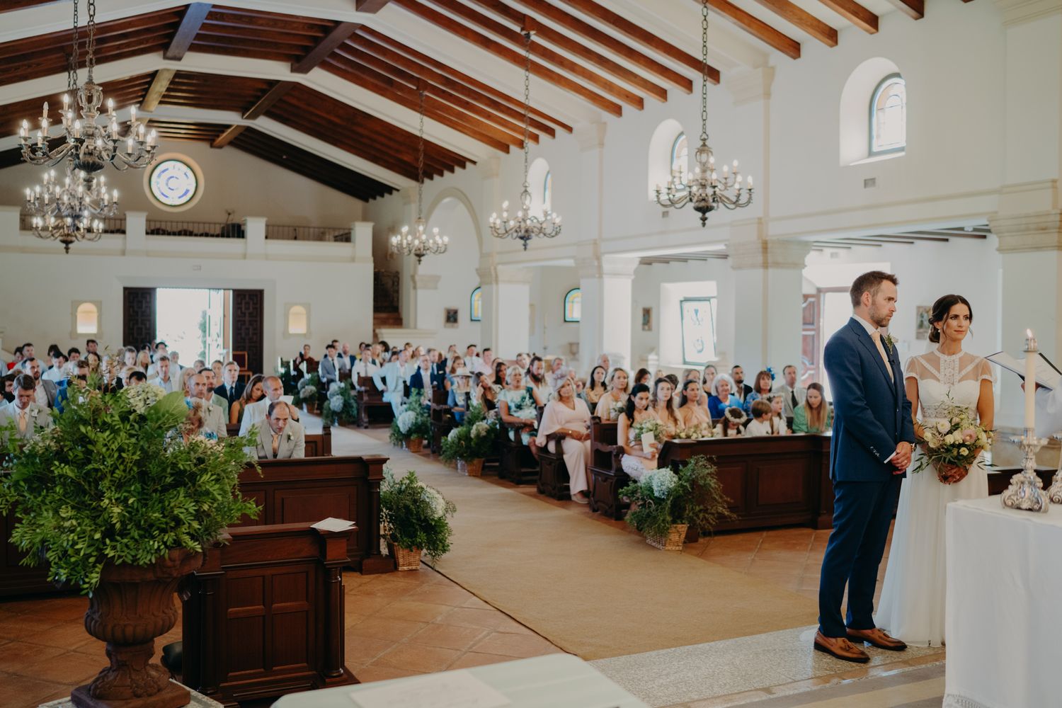 Elegant wedding ceremony in a grand hall with vaulted wooden beams, chandeliers and floral arrangements.