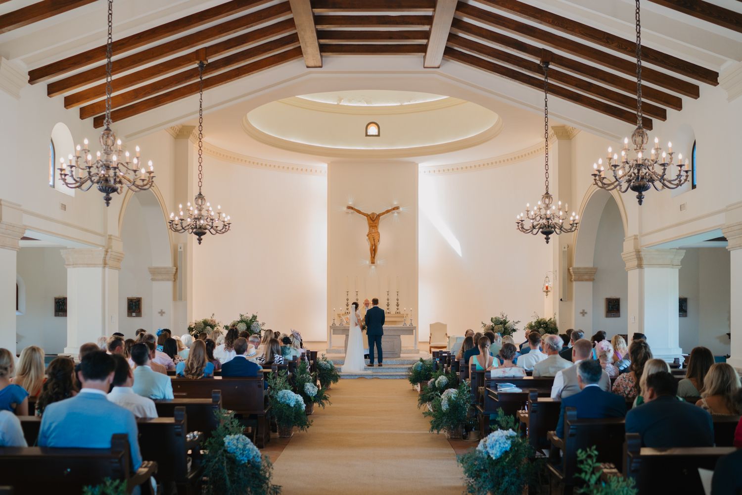 Church wedding ceremony with wooden beam ceiling and crystal chandeliers.