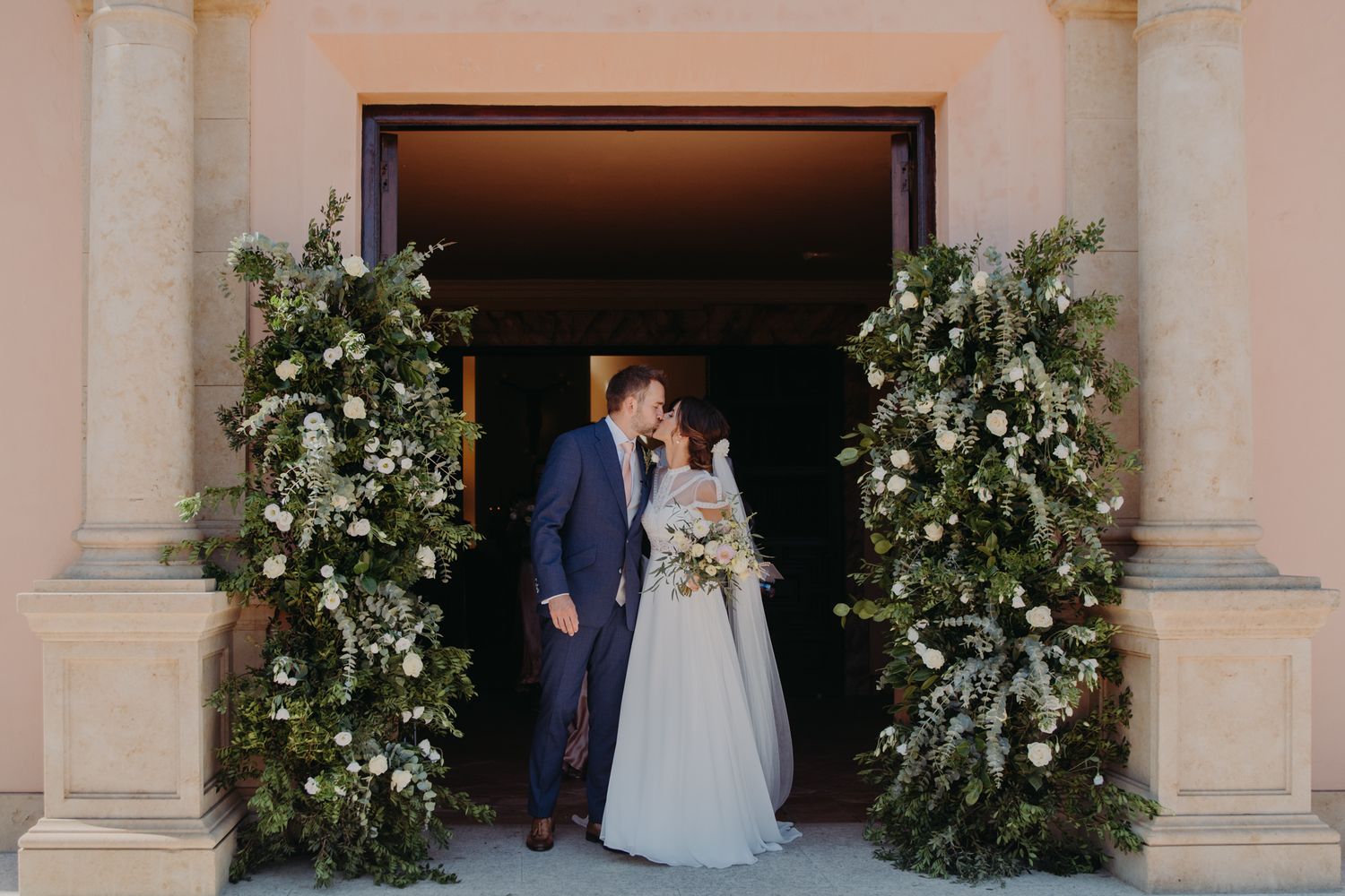 A couple shares a moment in a doorway decorated with lush white floral arrangements.