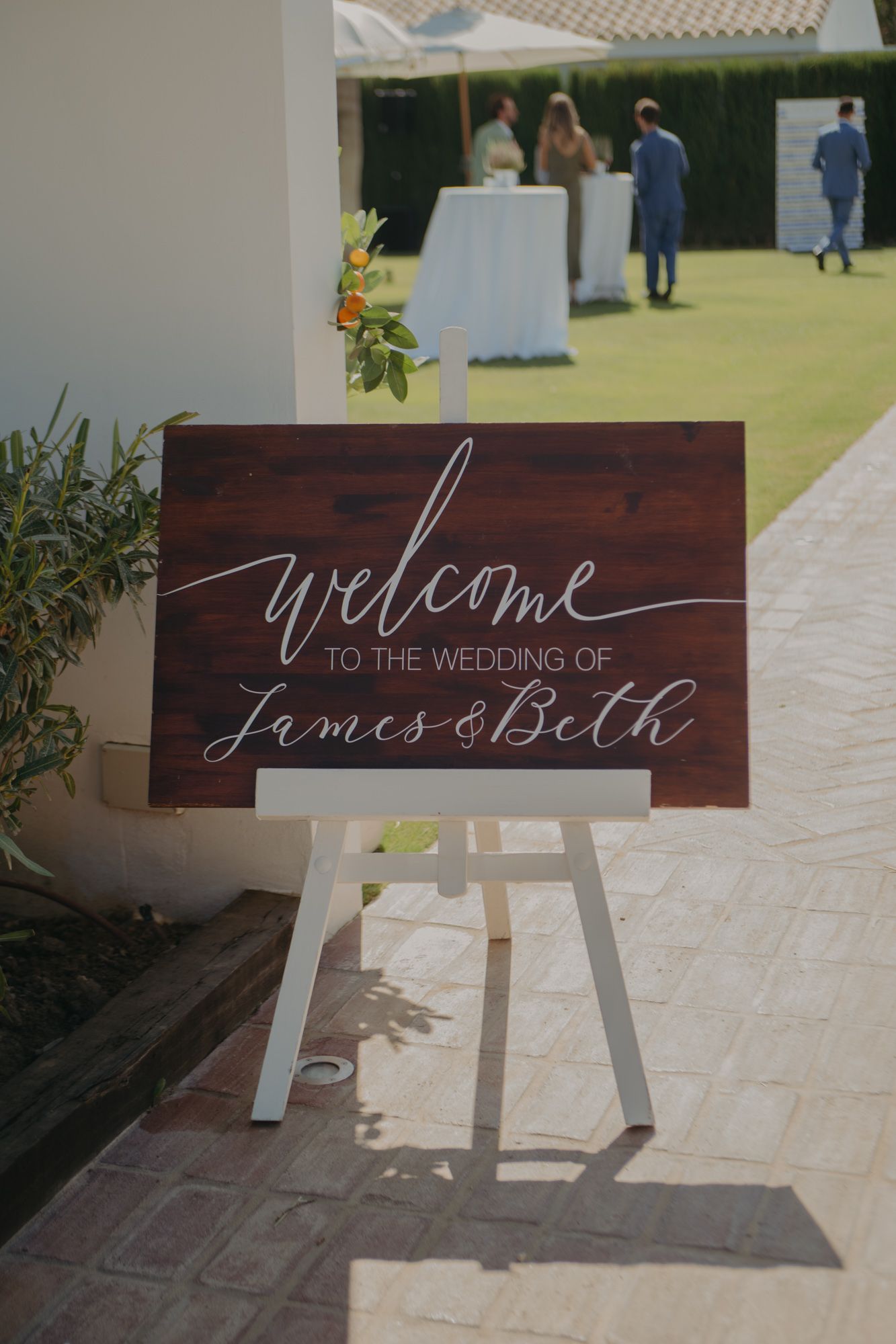 Wooden welcome sign on white easel displays elegant calligraphy for a wedding celebration.