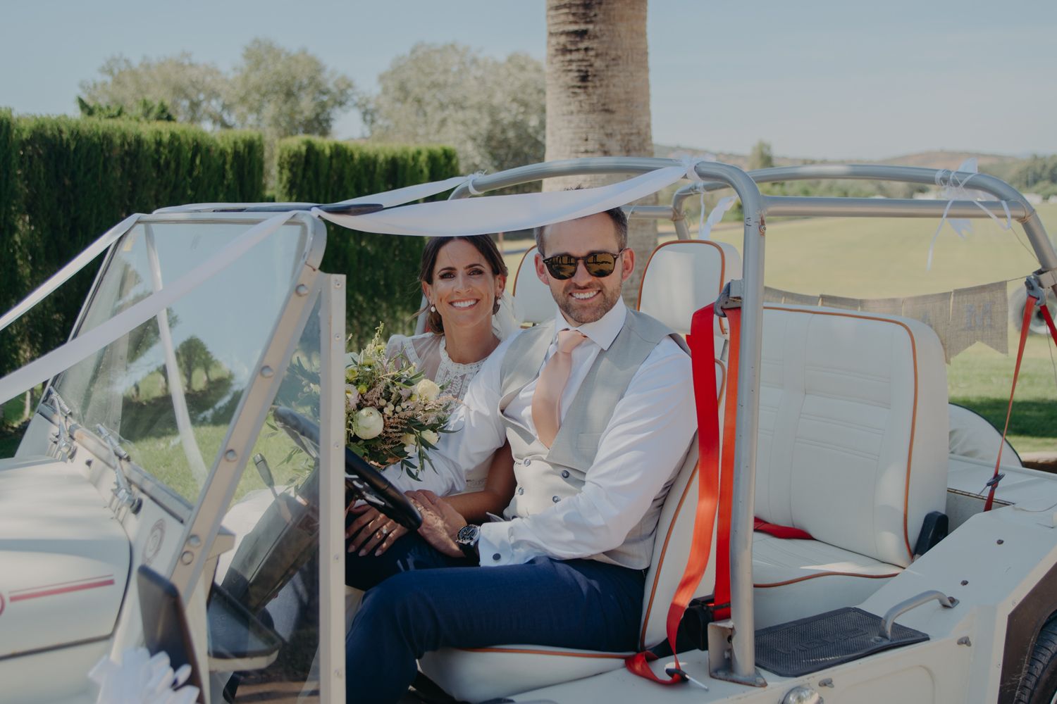 Happy couple sitting in a decorated golf cart at a wedding venue.
