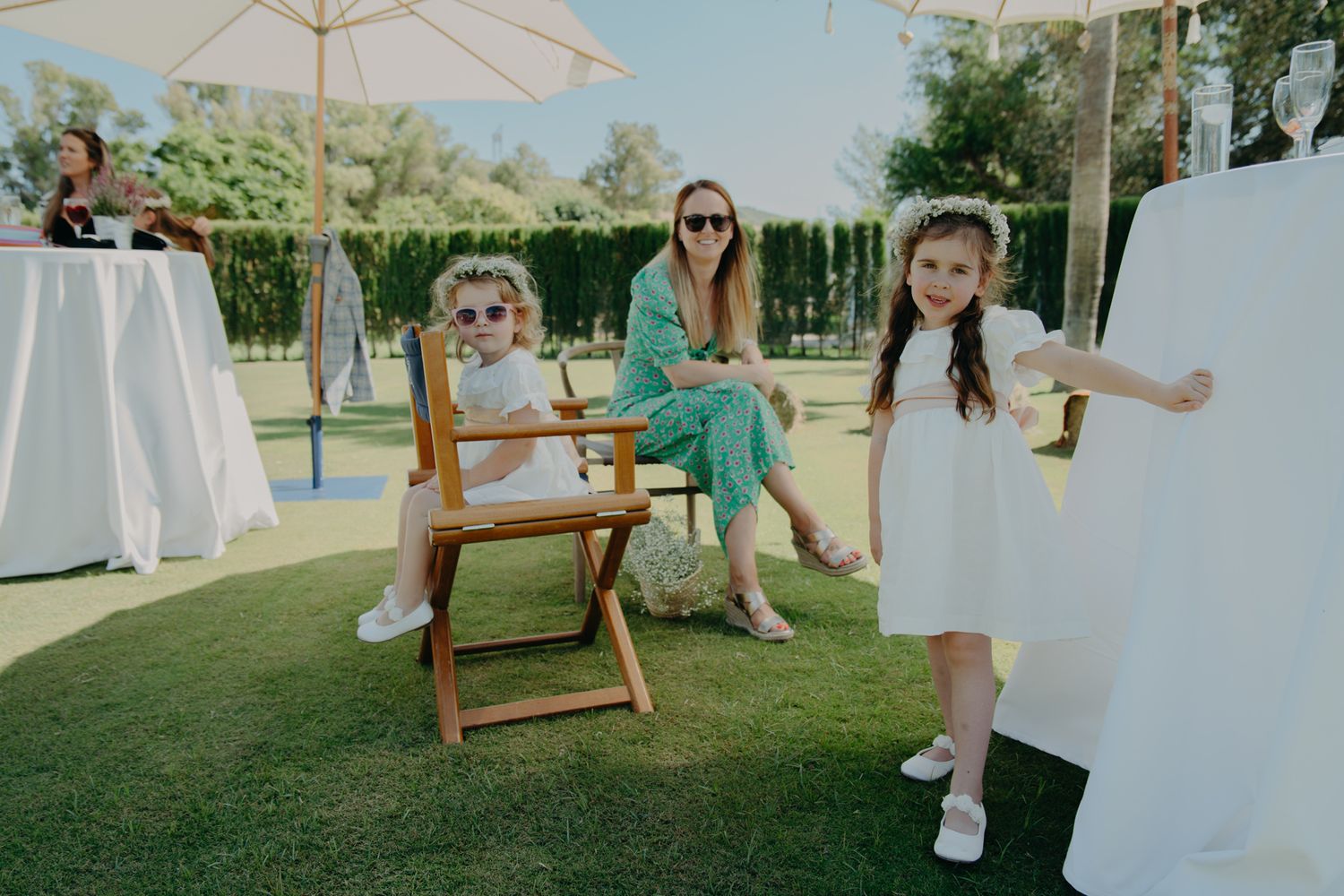 Wedding guests relaxing on outdoor furniture under an umbrella at a garden reception.