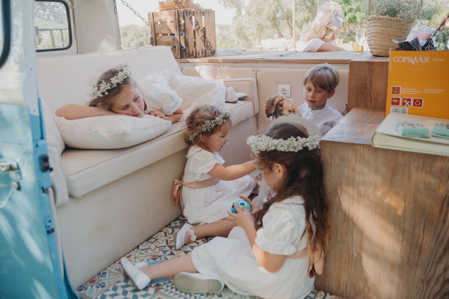 Group lounging inside a vintage camper van decorated with pillows and blankets on a sunny day.
