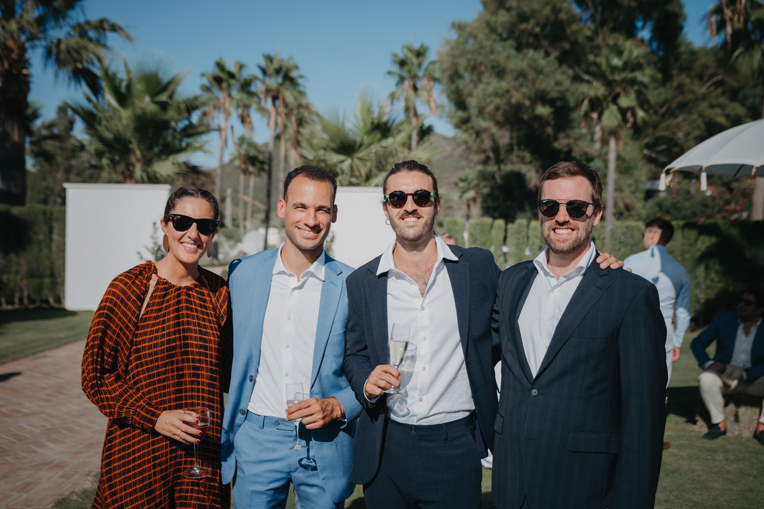 Guests in formal attire enjoying an outdoor celebration with palm trees in the background.