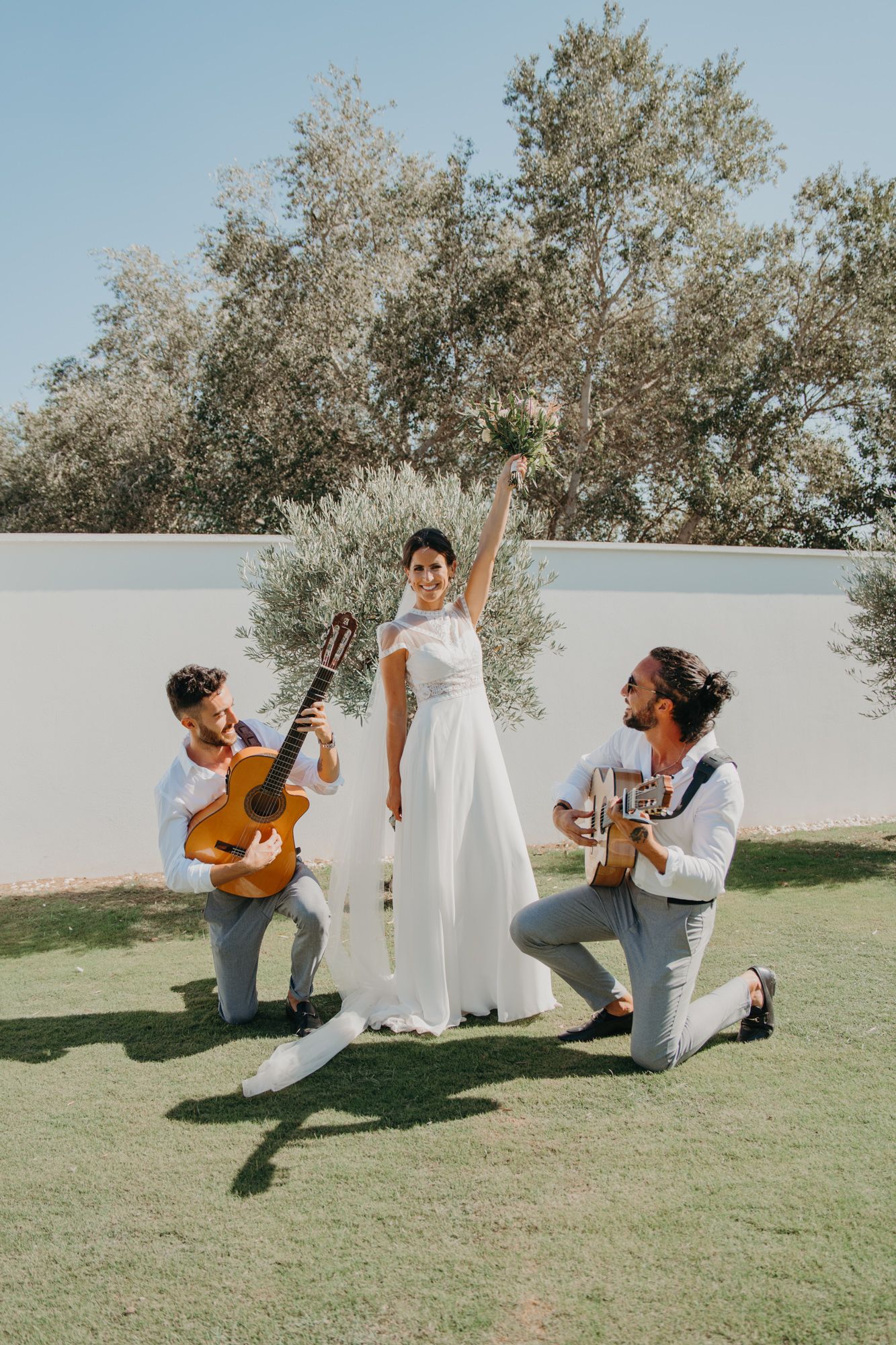 Musicians with guitars perform for the bride in an outdoor garden setting.
