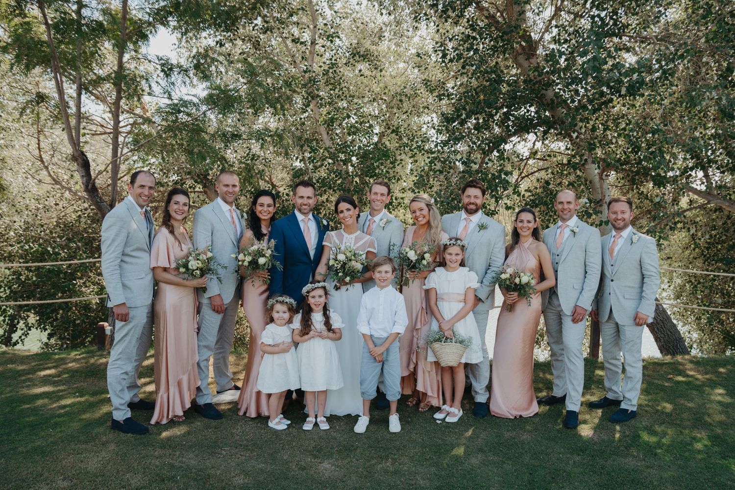 Wedding party members in pastel and light colored attire pose for group photo outdoors.