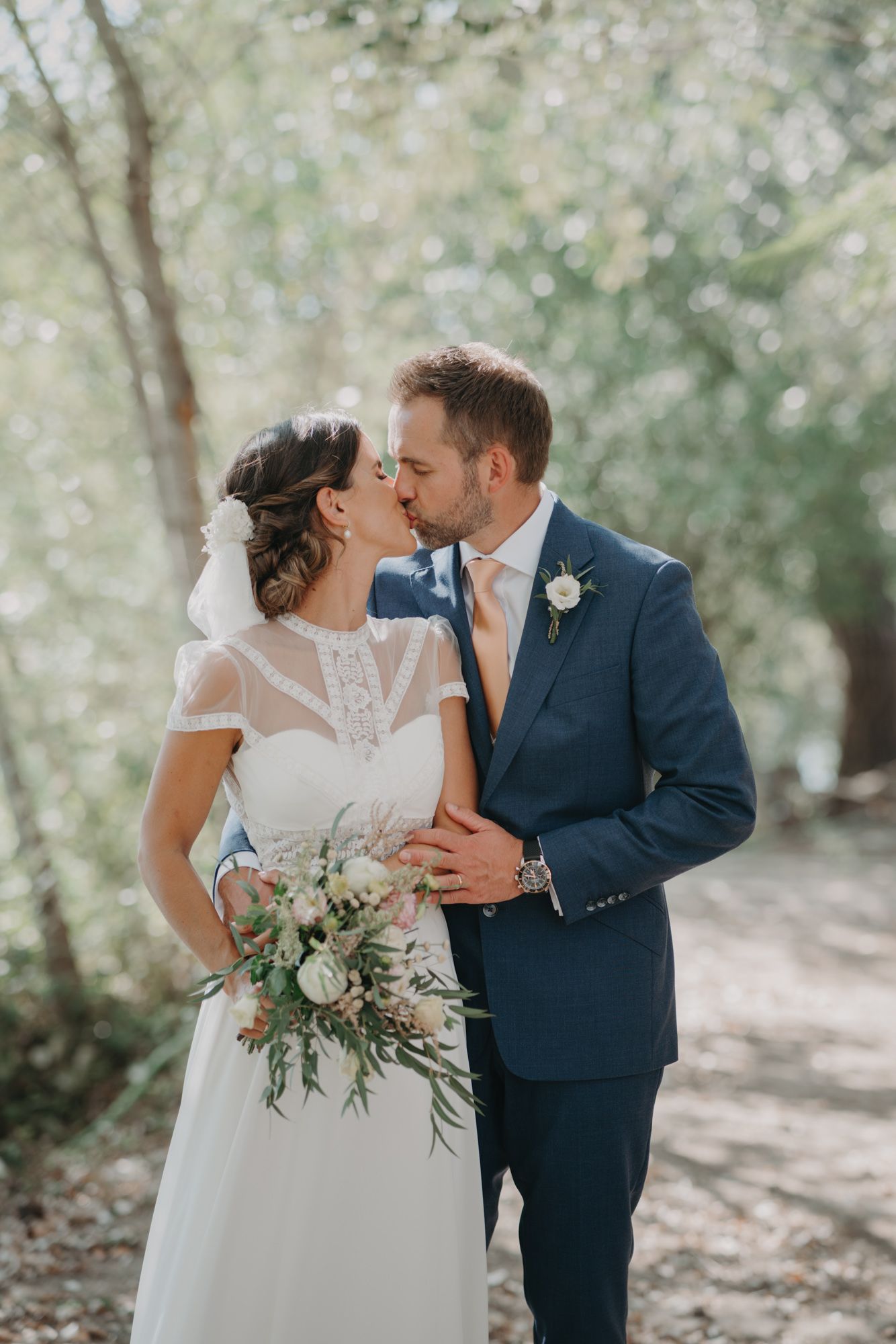 A romantic woodland wedding portrait showing a couple in elegant attire with a natural greenery bouquet.