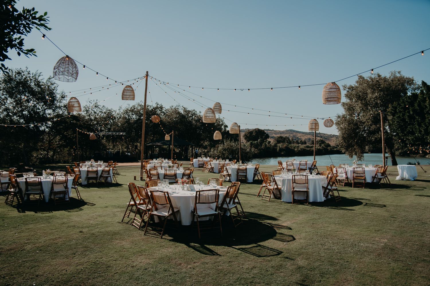 Outdoor wedding venue with string lights and round tables set up on grassy field.