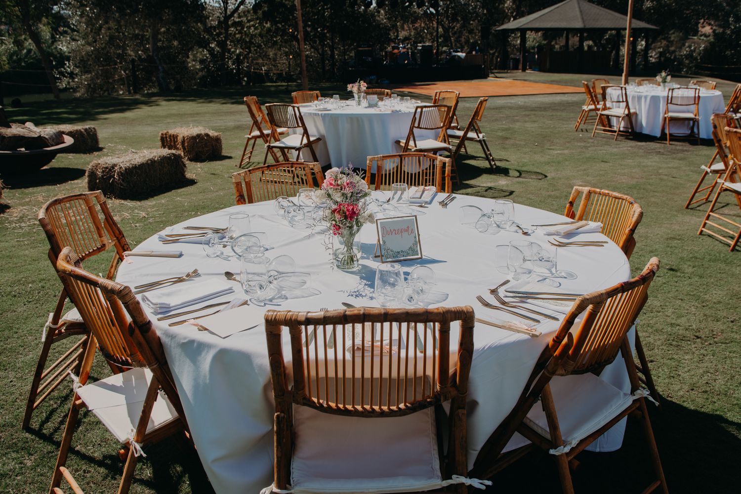 Outdoor wedding reception setup with round tables and wooden chairs on a lawn.