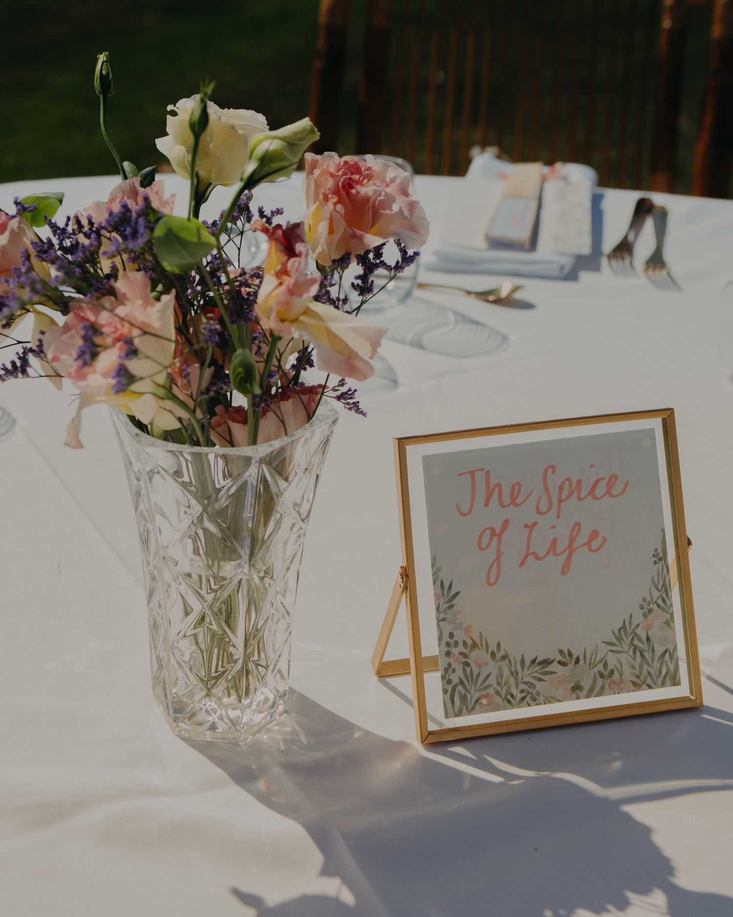 A wedding table detail with delicate floral centerpiece and 'The Spice of Life' sign.