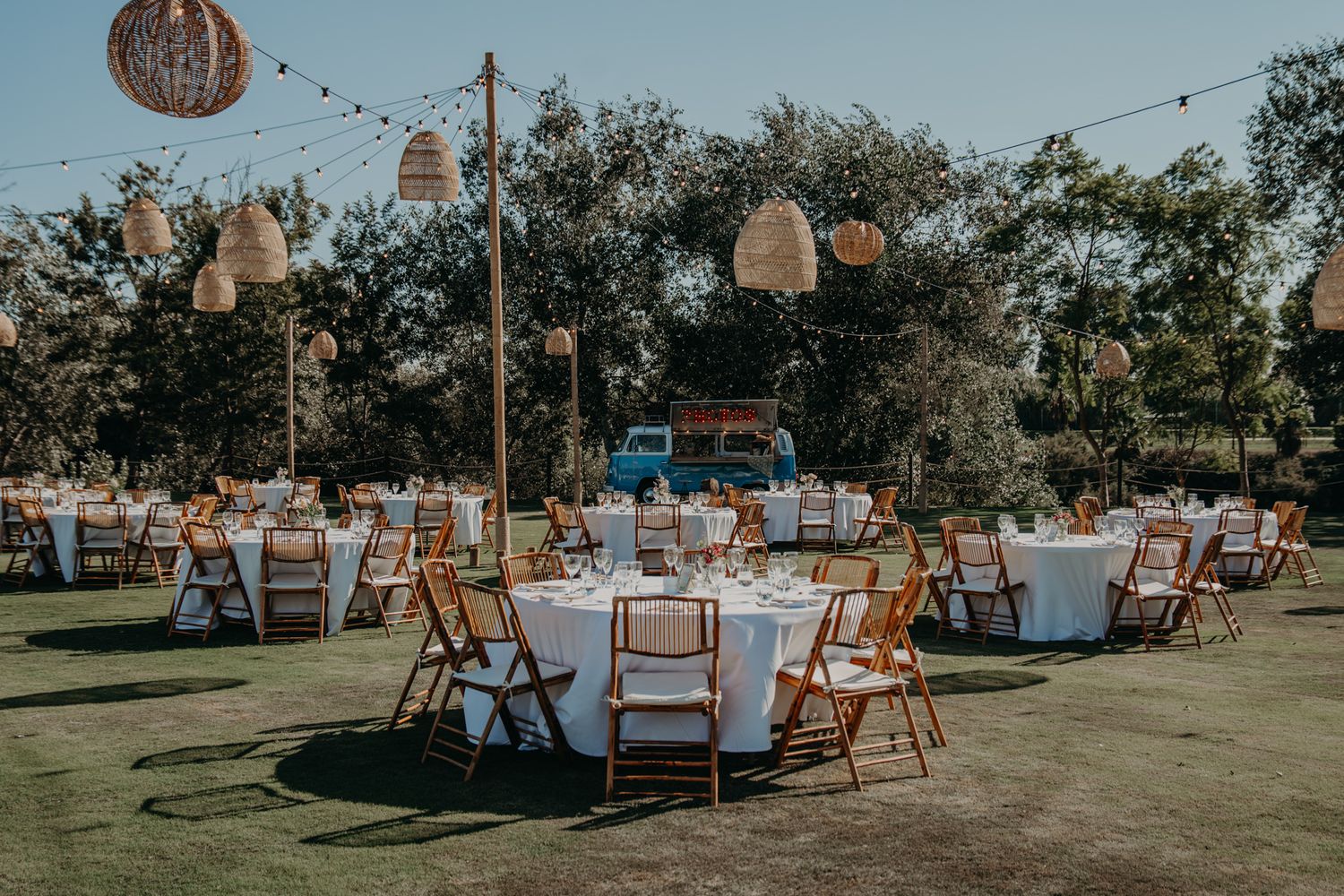 Outdoor wedding reception setup with round tables, folding chairs, and hanging lantern decorations.