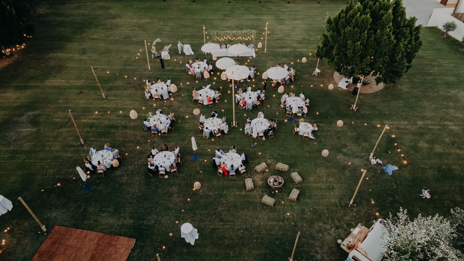 Aerial view of an outdoor wedding reception with white tables scattered across a green lawn.