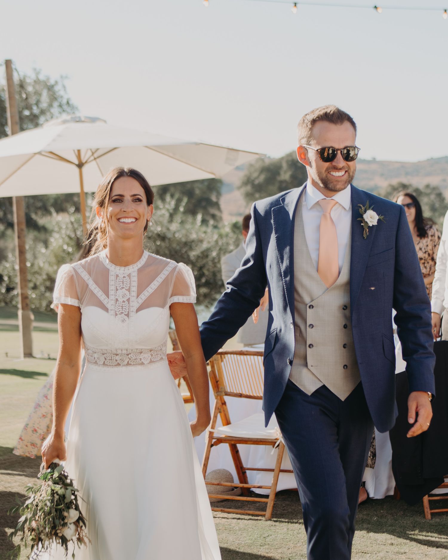 Elegant outdoor wedding celebration with couple in formal attire walking together on lawn.